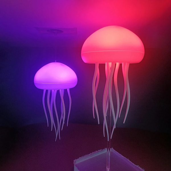 Luminária de medusa com cabeça iluminada em rosa e corpo em tentáculos ondulados, emitindo luz suave em um ambiente escuro.