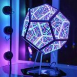 Luminária de mesa com estrutura geométrica iluminada por LEDs coloridos, com padrão de linhas e formas modernas, em ambiente escuro.