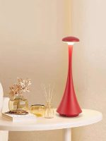Candeeiro de mesa vermelho com design elegante e base larga, colocado numa mesa branca junto a vasos decorativos e livros.