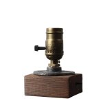 Microscópio antigo com corpo de metal dourado, base de madeira escura e ajuste de foco lateral, usado para observação científica.