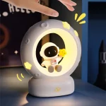 Luminária de astronauta sentado dentro de uma lua, segurando uma estrela amarela, com detalhes de luzes amarelas e uma base branca.