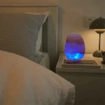 Lâmpada de sal com luz azul acesa numa mesa de cabeceira, ao lado de uma lâmpada de leitura, numa decoração de quarto relaxante.