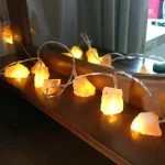 Luzes decorativas de sal de rocha em forma irregular, emitindo luz quente, colocadas numa superfície de madeira junto a um espelho.