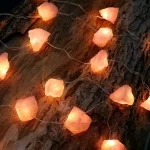 Luzes de LED em forma de pedras de sal, iluminando um tronco de árvore com casca rústica.