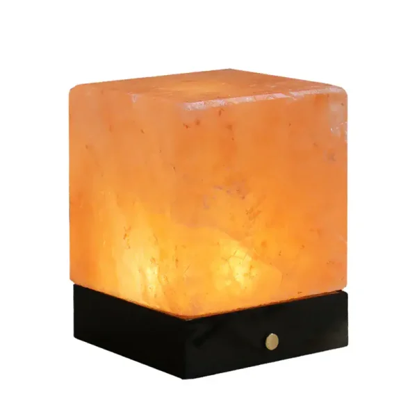 Lâmpada de sal de sal gema com base preta, iluminada, mostrando textura e cor laranja.