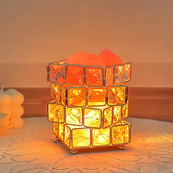 Luminária com estrutura de cubos de vidro laranja, iluminada por dentro, em ambiente acolhedor, com fundo neutro e superfície de madeira.