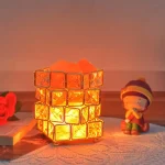 Lâmpada de plasma com cubos de vidro refletindo luz laranja, ao lado de uma figura de boneco com gorro colorido, em ambiente acolhedor.