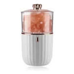 Moedor de sal de rocha rosa com corpo branco e detalhes dourados, mostrando o sal em pó sendo moído.