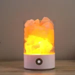 Lâmpada de plasma com nuvem de cores laranja e amarela, iluminação interna brilhante, base branca com botão de energia, sobre superfície de madeira.