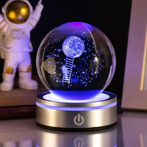 Globo de ciência com astronauta a subir uma escada até à lua, decorado com estrelas e planetas, iluminado por luz azul e roxa, em base metálica com botão de ligar.