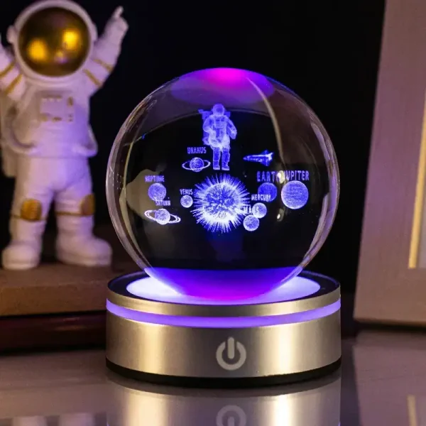 Globo de ciência com projeções de planetas, astronauta e estrelas, iluminado por luzes LED, sobre base metálica, ao lado de uma figura de astronauta de brinquedo.