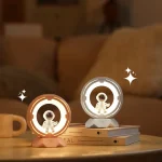 Luzes decorativas com astronautas em miniatura, uma com luz quente e outra com luz fria, colocadas sobre livros na mesa de um sofá.