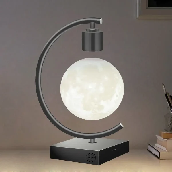 Lâmpada com base preta, estrutura metálica curva, e esfera que simula a lua, em ambiente interno com livros ao lado.