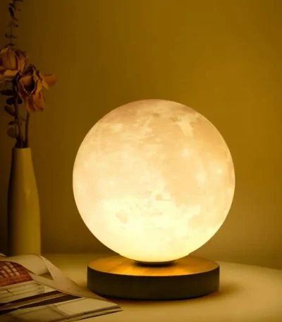 Lâmpada de lua decorativa com iluminação suave, colocada numa mesa ao lado de um vaso com flores secas e um livro aberto.