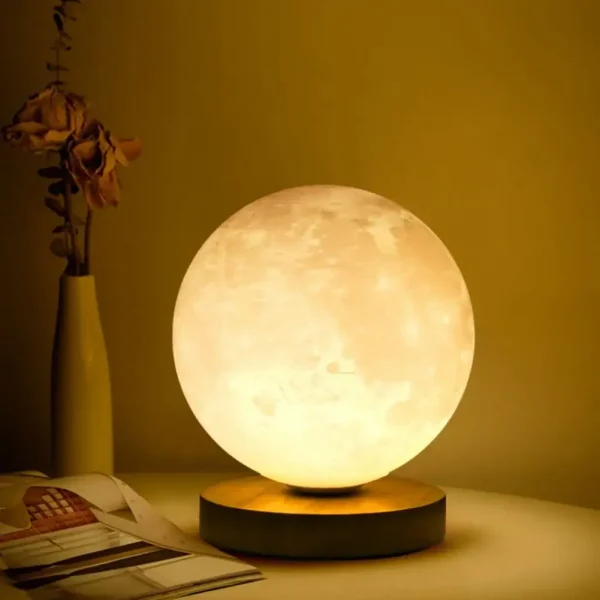 Lâmpada de lua decorativa com iluminação suave, colocada numa mesa ao lado de um vaso com flores secas e um livro aberto.