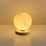 Lâmpada de lua decorativa com luz amarela suave, colocada sobre uma base circular de madeira, criando um efeito de lua realista.