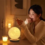 Jovem mulher sorridente a usar telemóvel ao lado de lâmpada lunar decorativa em ambiente acolhedor com velas acesas.