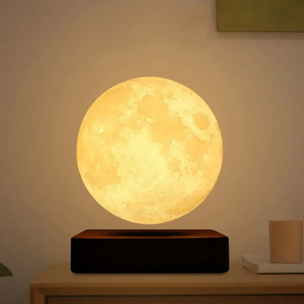 Lâmpada de luz amarela com forma de lua, colocada numa base preta sobre uma mesa de madeira clara, ambiente de sala moderna.