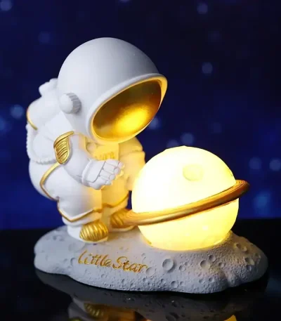 Miniatura de astronauta com capacete dourado a segurar um planeta LED brilhante, sobre base lunar com inscrição "Little Star".