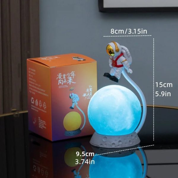 Candeeiro de mesa em forma de lua com figura de astronauta a segurar a luz, acompanhado de caixa de embalagem com design colorido e detalhes em chinês.