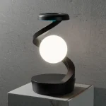 Lâmpada de mesa com base preta, braço curvo e esfera luminosa branca, sobre uma superfície de mármore.