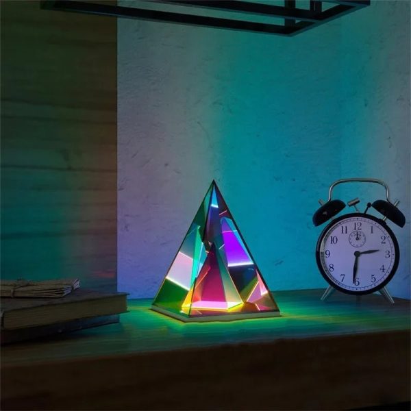 Pirâmide holográfica com luzes RGB coloridas, junto a um despertador clássico e livros numa mesa de madeira.
