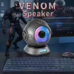 Altifalante de voz inspirado no personagem Venom, com design futurista e luzes LED coloridas, colocado numa secretária com teclado e rato.
