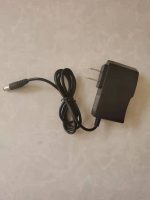 Fonte de alimentação com cabo ligado, usada para alimentar o disco de plasma azul, vista de cima com foco no conector e na tomada elétrica.