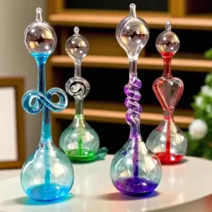 Conjunto de cinco tubos de vidro coloridos com formas variadas e detalhes decorativos, exibidos numa superfície branca com fundo de estantes de madeira.