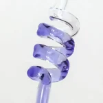 Espiral de vidro transparente com detalhes em azul e roxo, visto de lado, com fundo branco. Mostra a forma curva e o brilho do material.