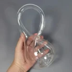 Vidro de laboratório de vidro transparente com curvas complexas, segurado por uma mão contra fundo cinzento.