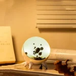 Lâmpada de plasma com esfera decorativa, mostrando descargas elétricas internas e base de suporte branca, colocada sobre uma mesa com livros e objetos de decoração.