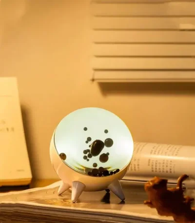 Lâmpada de plasma com esfera decorativa, mostrando descargas elétricas internas e base de suporte branca, colocada sobre uma mesa com livros e objetos de decoração.