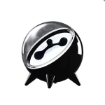 Relógio de mesa preto com visor oval e três patas de suporte, com detalhes em branco e preto, estilo moderno e minimalista.