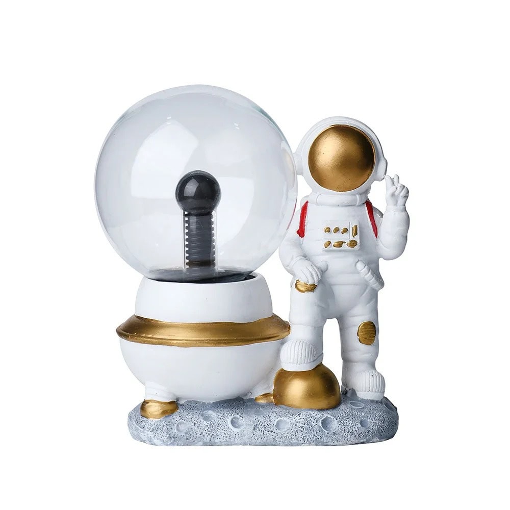 Decoração de ciência com astronauta e globo de luz Figura decorativa de astronauta com traje branco, detalhes dourados, junto a um globo de plasma com base branca e dourada, sobre uma superfície de imitação de lua.