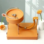 Pista de rolamento de metal com bolas de aço, com duas flores decorativas ao lado, fundo claro com sombra de plantas.