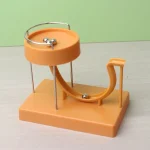 Dispositivo de física com esfera metálica, tubo curvo e base de plástico laranja, usado para demonstrações científicas educativas.