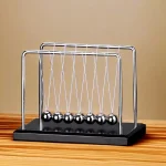 Pêndulo de Newton com bolas metálicas suspensas por fios, em uma base preta, sobre uma mesa de madeira, fundo neutro.