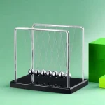 Pêndulo de Newton com bolas de metal suspensas por fios finos, em fundo verde, sobre base preta, demonstrando leis da física.