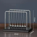 Pêndulo de Newton com cinco bolas de metal suspensas por fios finos, apoiado numa base preta, medindo 17cm de altura, 23cm de comprimento e 14cm de profundidade.