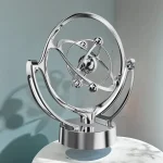 Modelo de átomo decorativo em metal com órbitas e partículas metálicas brilhantes, colocado sobre uma base circular.