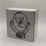 Modelo de átomo de plasma com esferas metálicas e anéis, em embalagem de papelão.