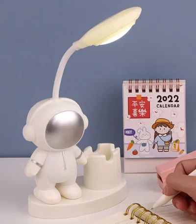 Luminária de mesa com cabeça de robô, braço flexível com lâmpada, ao lado de calendário de 2022 e caderno de notas com caneta.