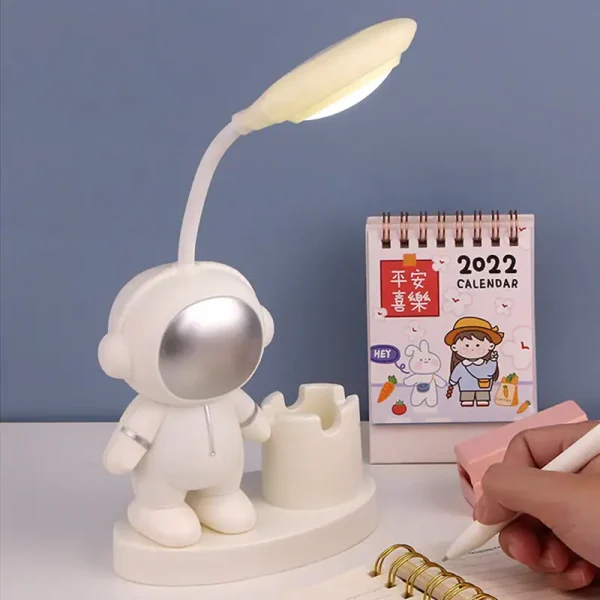 Luminária de mesa com cabeça de robô, braço flexível com lâmpada, ao lado de calendário de 2022 e caderno de notas com caneta.
