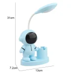 Luminária de mesa com corpo de astronauta azul, cabeça com visor preto e braço articulado com luz LED, base com suporte para acessórios.
