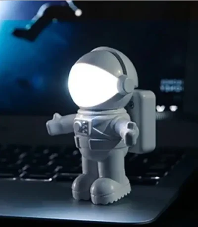 Miniatura de astronauta com capacete iluminado por luz LED branca, com detalhes em cinza e mochila, colocado sobre um portátil preto.