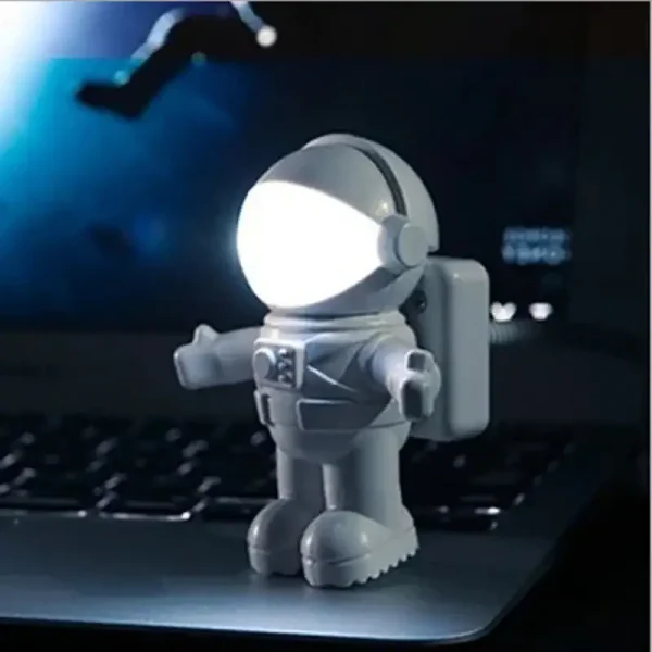 Miniatura de astronauta com capacete iluminado por luz LED branca, com detalhes em cinza e mochila, colocado sobre um portátil preto.