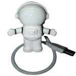 Robô de brinquedo em forma de astronauta com corpo branco, capacete e braços articulados, conectado a um cabo USB para carregamento ou funcionamento.