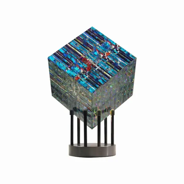 Escultura de vidro com padrões coloridos e textura brilhante, apoiada em suporte de metal com base circular.