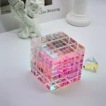 Cubo de vidro translúcido com estrutura em grade, iluminado com luz rosa, acompanhado de uma pirâmide de vidro ao lado, decorativo e científico.